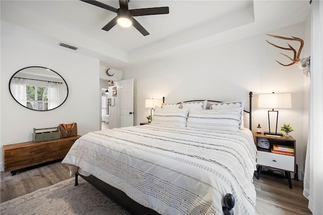 bedroom featuring a ceiling fan, baseboards, wood finished floors, a tray ceiling, and visible vents