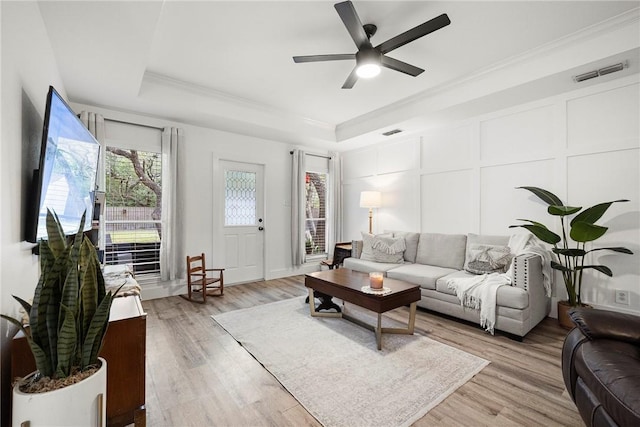living room featuring visible vents, crown molding, ceiling fan, light wood-type flooring, and a tray ceiling