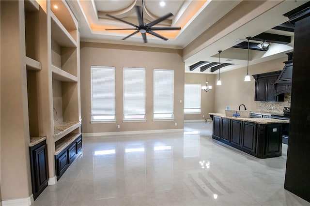 kitchen featuring ceiling fan, light stone counters, ornamental molding, an island with sink, and decorative light fixtures