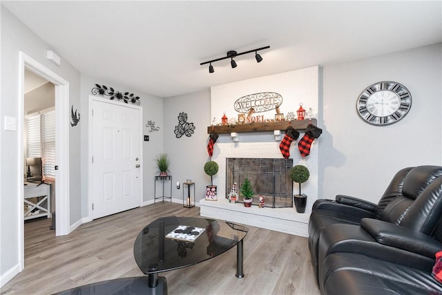 living room with rail lighting, a brick fireplace, and light wood-type flooring