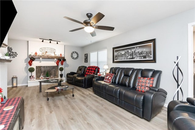 living room with a fireplace, track lighting, ceiling fan, and light wood-type flooring