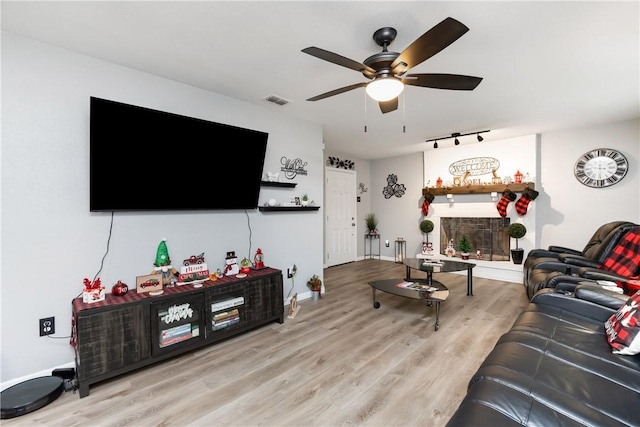 living room featuring ceiling fan, track lighting, a fireplace, and light wood-type flooring