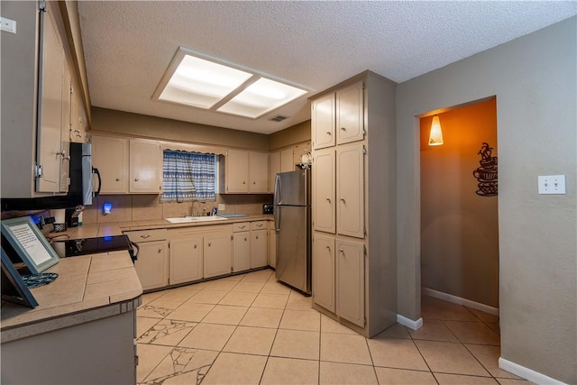 kitchen featuring sink, a textured ceiling, light tile patterned floors, stainless steel refrigerator, and range