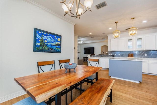 dining area featuring light wood-style floors, crown molding, ceiling fan with notable chandelier, and visible vents