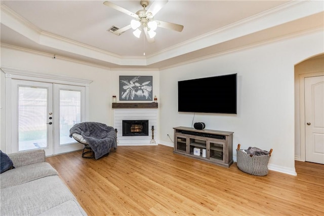 living room featuring visible vents, a tray ceiling, french doors, a fireplace, and light wood finished floors