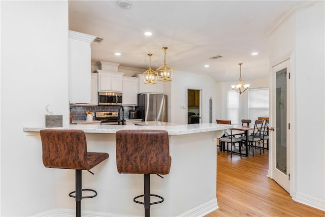 kitchen with backsplash, a breakfast bar area, appliances with stainless steel finishes, a peninsula, and white cabinetry