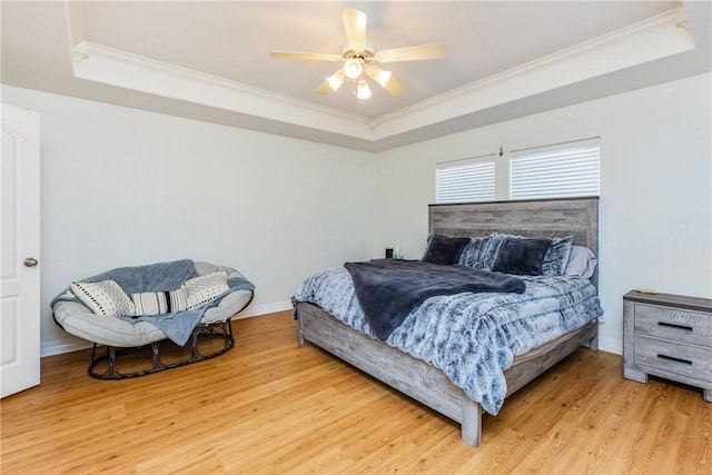 bedroom with a raised ceiling, crown molding, and light wood-type flooring