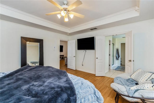 bedroom with light wood finished floors, visible vents, a raised ceiling, and crown molding