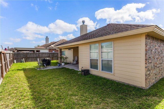 back of house featuring brick siding, a lawn, a chimney, a fenced backyard, and a patio area