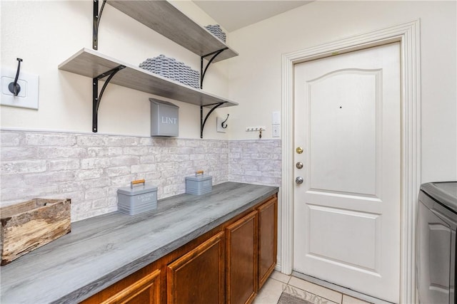 kitchen featuring open shelves, dark countertops, brown cabinetry, light tile patterned floors, and washer / dryer