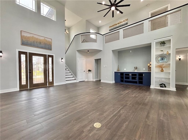 unfurnished living room featuring a high ceiling, built in features, ceiling fan, and dark wood-type flooring