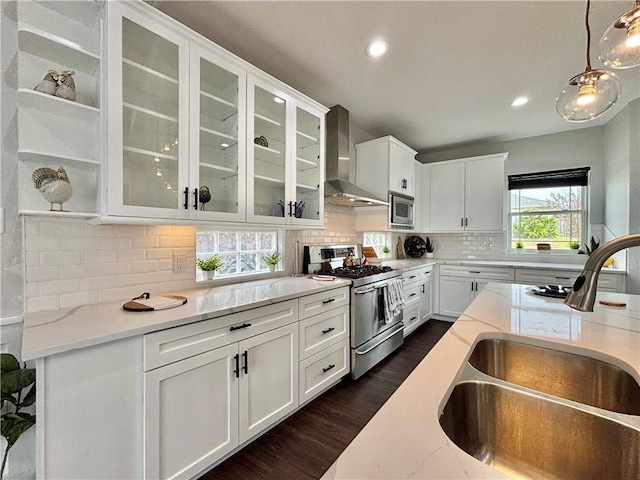 kitchen with pendant lighting, sink, wall chimney exhaust hood, light stone countertops, and appliances with stainless steel finishes