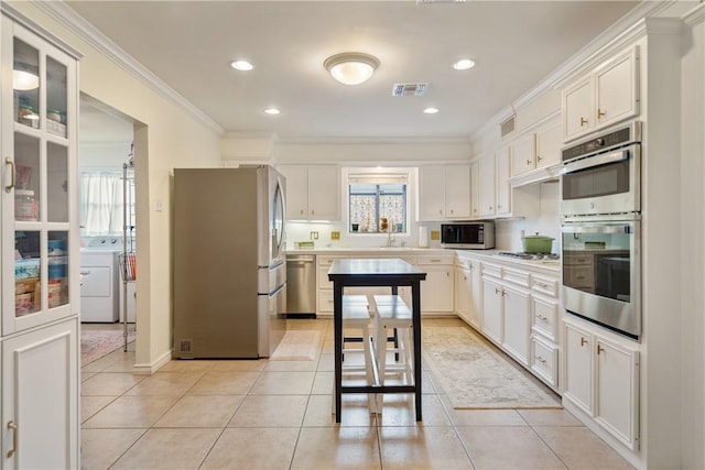 kitchen with separate washer and dryer, stainless steel appliances, visible vents, light tile patterned flooring, and crown molding