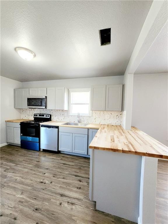 kitchen with kitchen peninsula, stainless steel appliances, butcher block countertops, white cabinetry, and sink