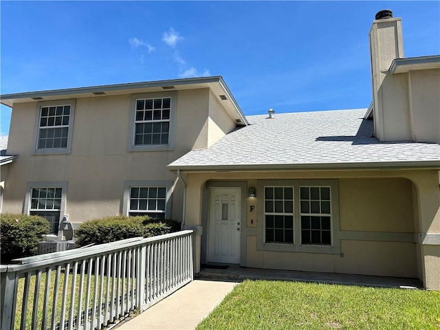 entrance to property with a shingled roof, a chimney, fence, and stucco siding