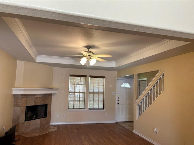 unfurnished living room featuring baseboards, a tiled fireplace, wood finished floors, a tray ceiling, and crown molding