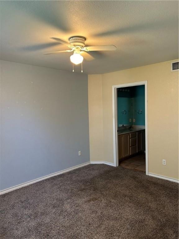 empty room featuring dark colored carpet, visible vents, ceiling fan, a textured ceiling, and baseboards