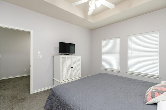 bedroom with ceiling fan, dark carpet, and a tray ceiling