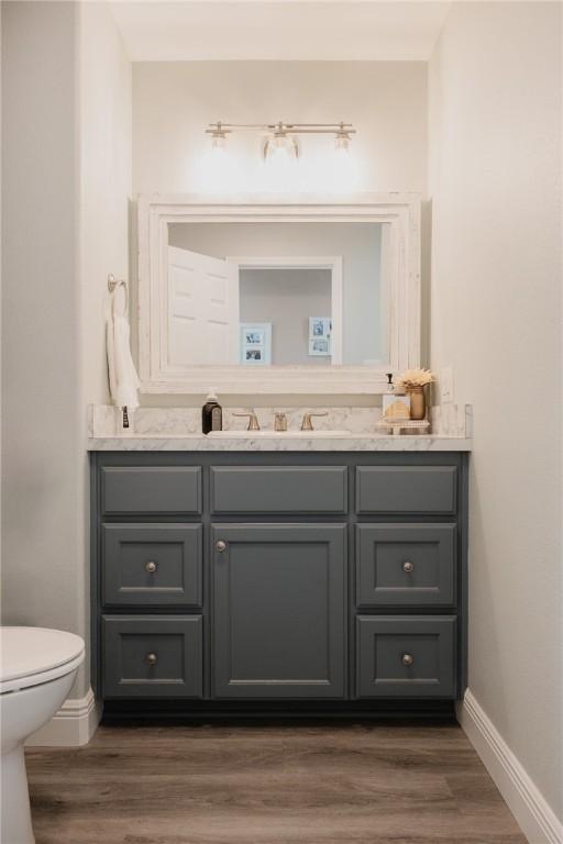 299 Bay Dr, Palacios, TX 77465 - half bathroom with vanity, baseboards, toilet, and wood finished floors