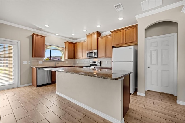 kitchen featuring visible vents, a center island, appliances with stainless steel finishes, dark stone counters, and decorative backsplash