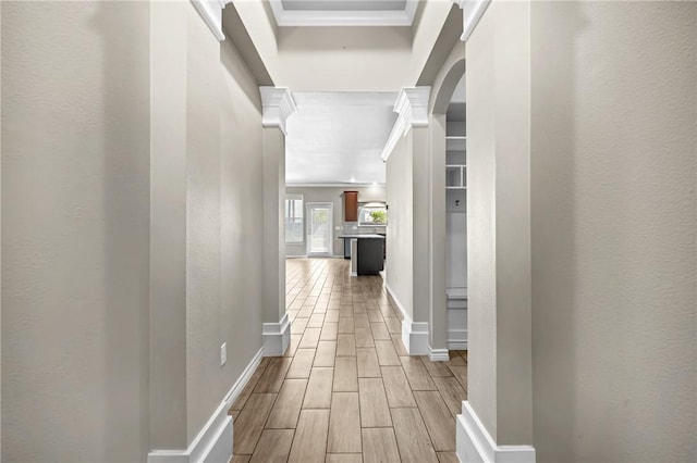 hallway with baseboards, ornamental molding, a textured wall, wood tiled floor, and arched walkways