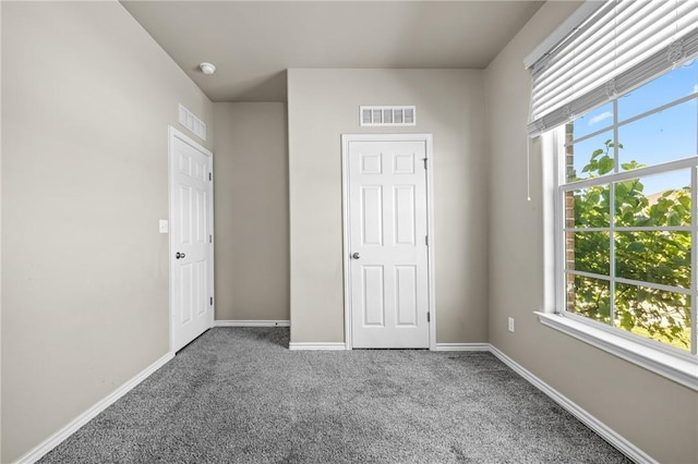 unfurnished bedroom with baseboards, multiple windows, carpet, and visible vents
