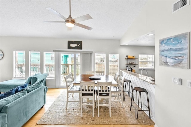 dining area with visible vents, light wood-style flooring, ceiling fan, vaulted ceiling, and a textured ceiling