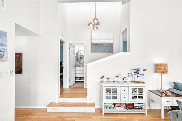 interior space featuring a towering ceiling, light wood finished floors, visible vents, and baseboards