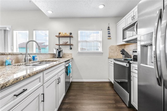 kitchen with a sink, white cabinetry, appliances with stainless steel finishes, light stone countertops, and tasteful backsplash