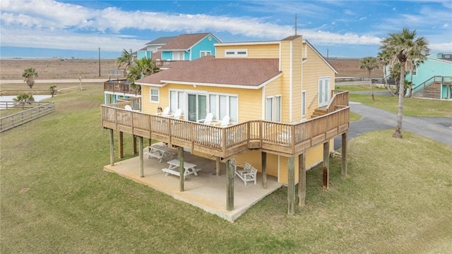 back of house featuring a deck, a patio, a yard, and roof with shingles