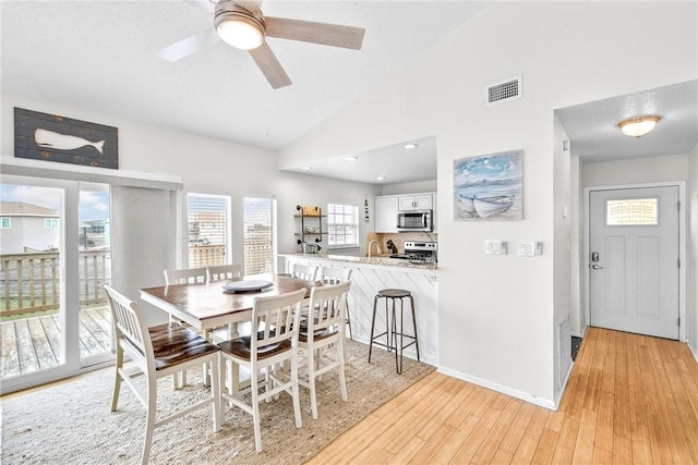 dining space featuring lofted ceiling, a textured ceiling, light wood-style flooring, visible vents, and baseboards