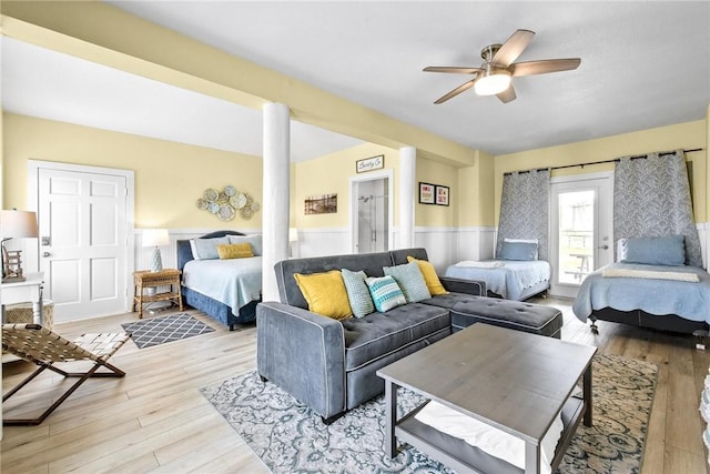 bedroom with access to outside, a ceiling fan, wainscoting, light wood-type flooring, and ornate columns