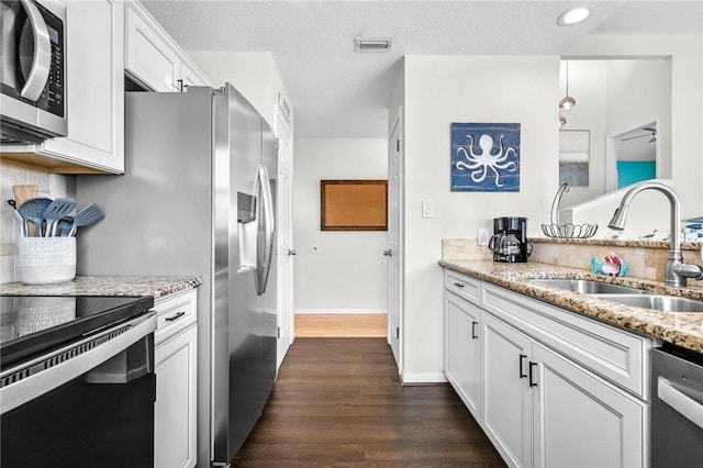 kitchen with light stone counters, stainless steel appliances, visible vents, white cabinetry, and a sink