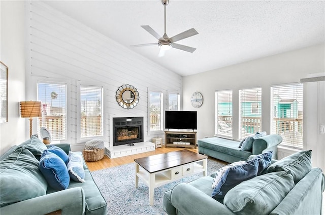 living area with a wealth of natural light, a textured ceiling, a fireplace with raised hearth, and wood finished floors