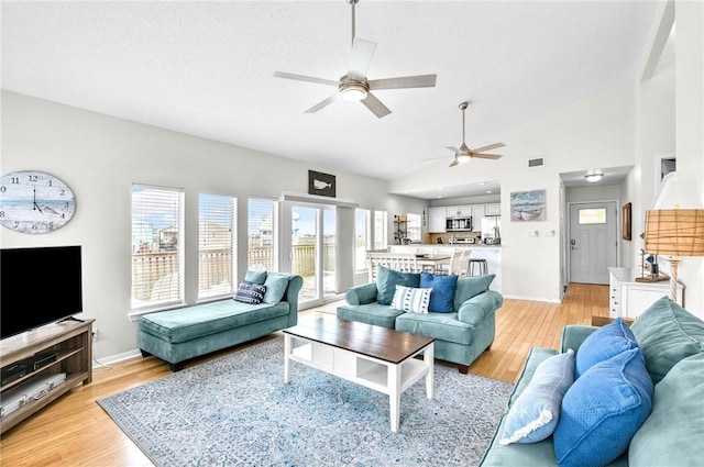 living area with high vaulted ceiling, light wood-style flooring, baseboards, and a ceiling fan