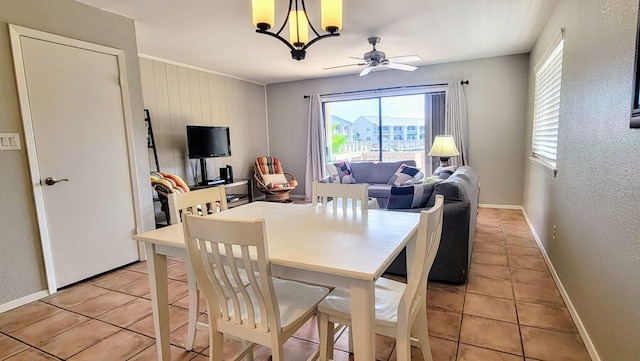 dining area with a textured wall, ceiling fan with notable chandelier, baseboards, and light tile patterned flooring