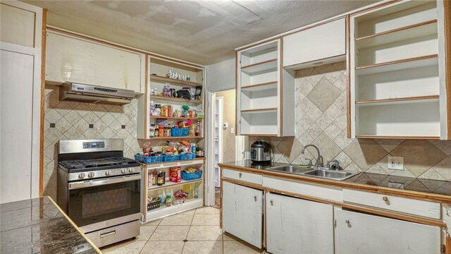 kitchen with sink, stainless steel range with gas cooktop, light tile patterned flooring, backsplash, and white cabinetry