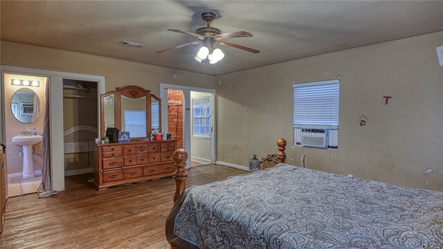 bedroom featuring light hardwood / wood-style floors, cooling unit, sink, connected bathroom, and ceiling fan