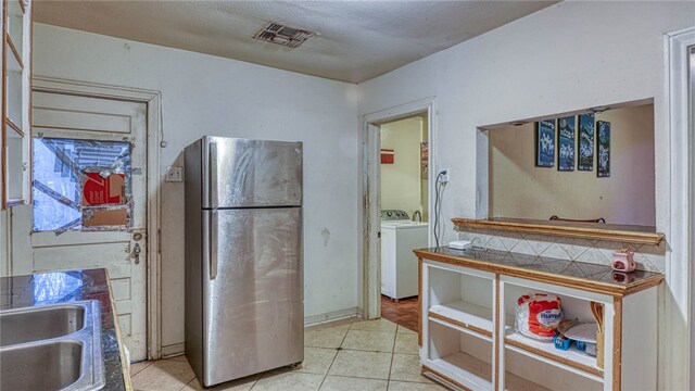 kitchen with light tile patterned flooring, stainless steel refrigerator, sink, a textured ceiling, and washer and clothes dryer