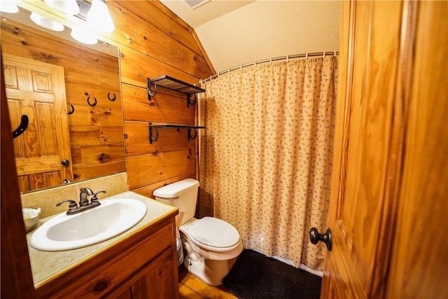 bathroom with toilet, vaulted ceiling, wooden walls, and vanity