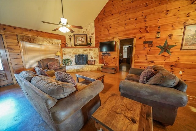 living room featuring ceiling fan, a stone fireplace, high vaulted ceiling, and wood walls