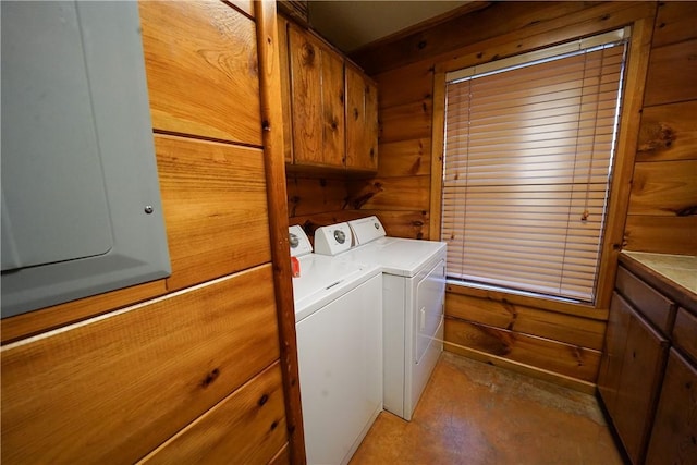 laundry area featuring electric panel, wood walls, cabinets, and separate washer and dryer