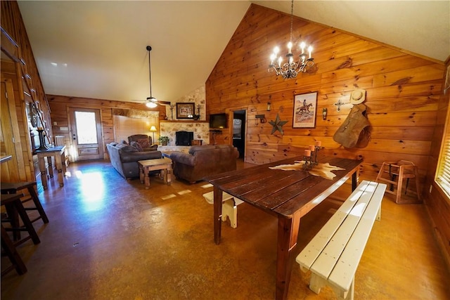 dining space featuring ceiling fan with notable chandelier, high vaulted ceiling, and a stone fireplace