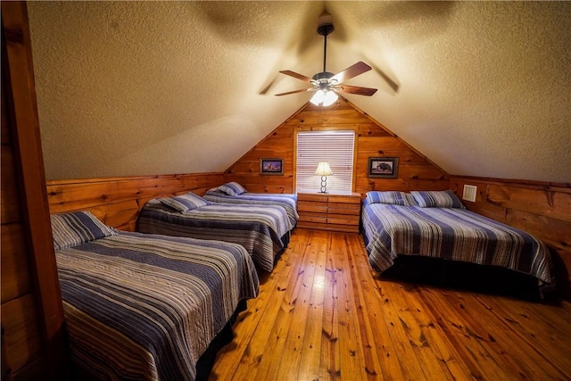 bedroom featuring ceiling fan, light hardwood / wood-style floors, wooden walls, and vaulted ceiling