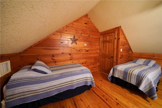 bedroom with lofted ceiling, a textured ceiling, wood walls, and wood-type flooring