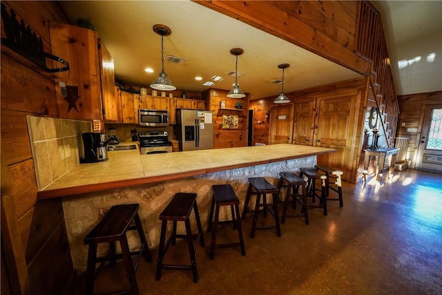 kitchen with kitchen peninsula, wooden walls, a breakfast bar, appliances with stainless steel finishes, and sink