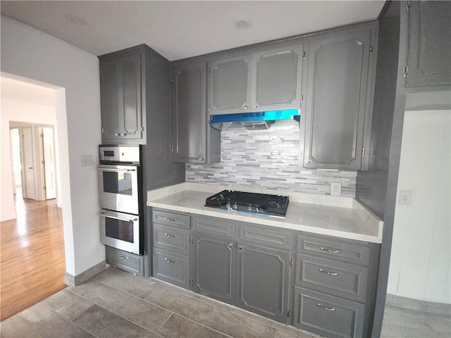 kitchen featuring stainless steel appliances, light tile patterned floors, decorative backsplash, and gray cabinetry