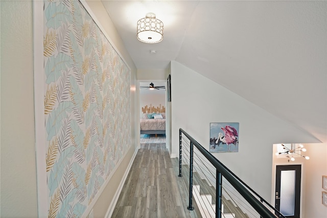 hallway with a notable chandelier, wood-type flooring, and vaulted ceiling