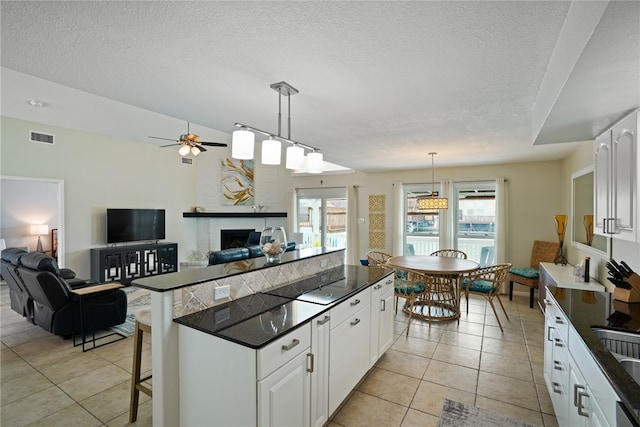 kitchen featuring a kitchen bar, pendant lighting, a textured ceiling, white cabinetry, and a large fireplace