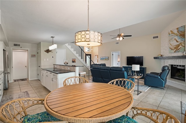 dining space with a fireplace, ceiling fan, light tile patterned floors, and vaulted ceiling